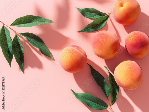 Fresh peaches and green leaves arranged on a pink background in a simple and vibrant composition