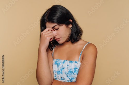 portrait of young girl rests her head on her hand, lost in thought. This image depicts contemplation on beige background