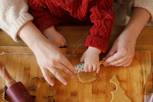 Mother with cute baby making gingerbread christmas cookies together, holding little rolling pin in hands close up, top view. Christmas family traditions, winter holiday preparation