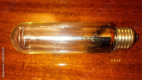 A clear, cylindrical high-pressure sodium lamp bulb resting horizontally on a dark wooden surface