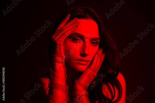 Portrait of a young brunette woman illuminated by red light in a mysterious and stylish background