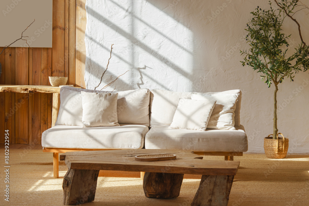 Fototapeta premium Bright cozy living room with light beige sofa, rustic wooden coffee table and sunlight streaming through window. Home interior design in scandinavian style with warm tones and natural materials.
