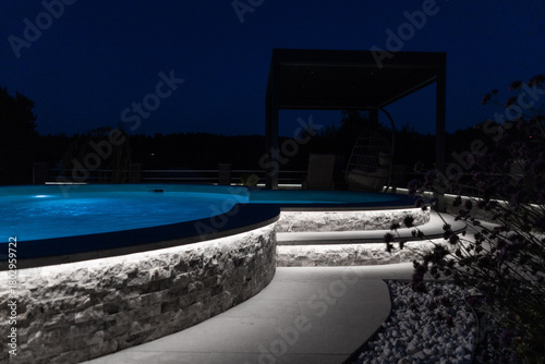 A modern outdoor pool glowing at night with vibrant LED lighting inside and around the water, creating a luxurious, serene, and atmospheric scene ideal for relaxation and nightlife visuals.