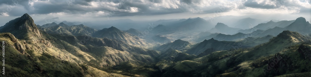 Fototapeta premium Aerial view of a vast mountain range under a cloudy sky with sunlight breaking through the clouds