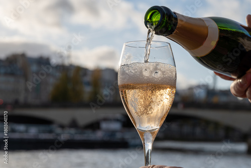 Pouring and drinking of french sparkling wine champagne from tulip glasses with view on Paris streets, buildings, Seine river embarkment, boats, bridges, wedding event in Paris