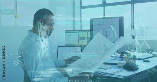 Examining architect in light-blue shirt and glasses, reviewing blueprints at office with monitors