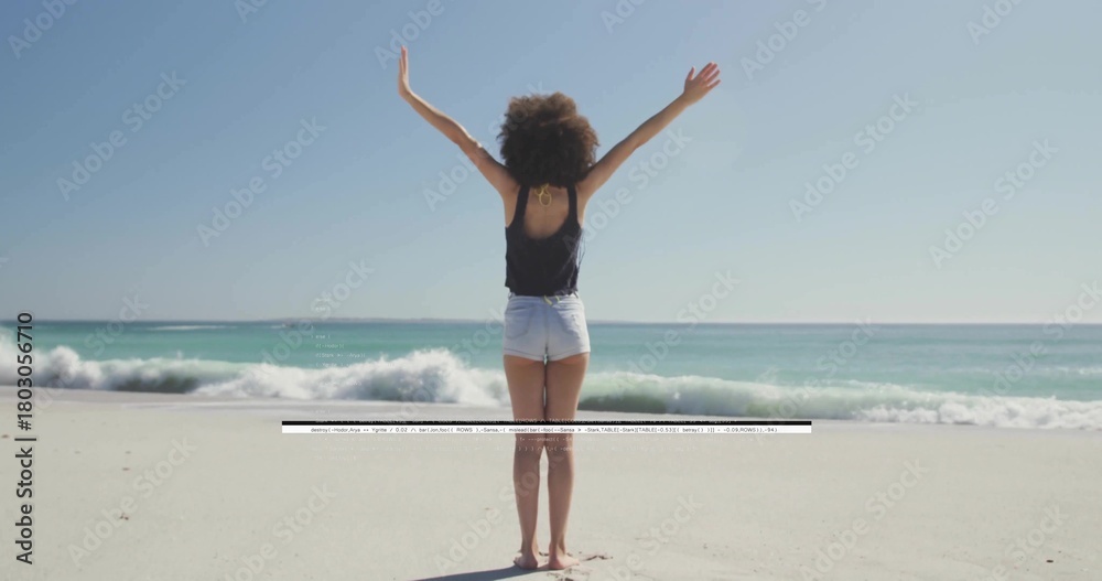 Naklejka premium Standing woman raising arms on beach in black tank top and shorts, waves, artifact crossing frame