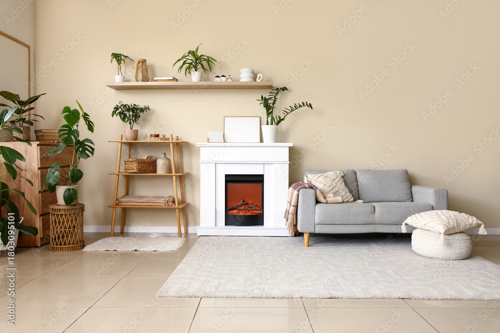 Fototapeta premium Interior of living room with fireplace, shelving unit and grey sofa near beige wall