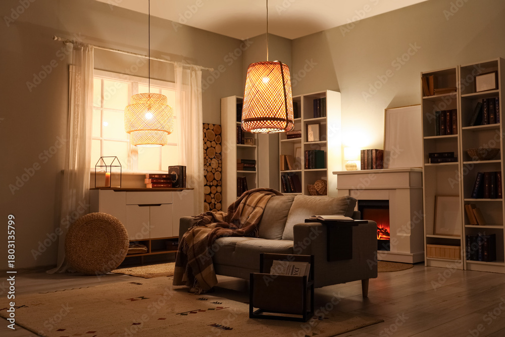 Fototapeta premium Interior of stylish living room with grey sofa, fireplace and bookshelves at evening