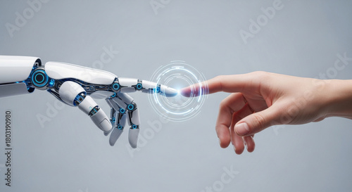Close-up of a human hand touching a robotic hand on a gray backdrop with a glowing digital interface, illustrating futuristic interaction and artificial intelligence concepts. 