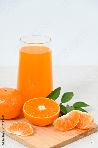 A glass of freshly squeezed orange juice, orange slices with whole oranges, and orange leaves in an organic basket on a white background.