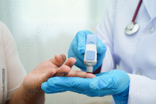 Asian woman self testing to check blood sugar level diabetes by digital lancet on finger at home.