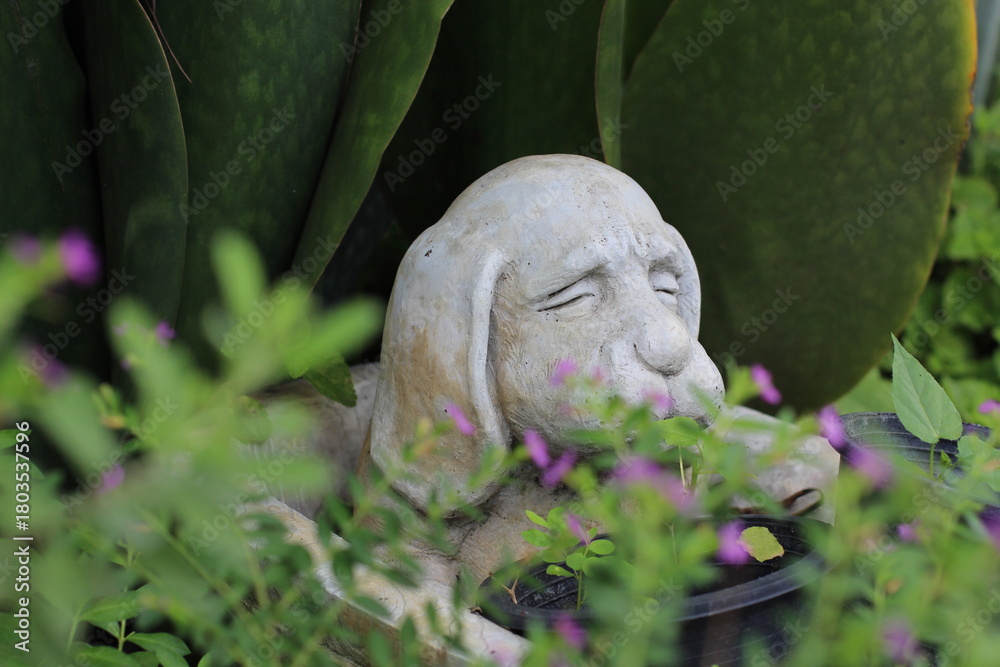 Obraz premium stone dog statue in a garden, surrounded by greenery and flowers