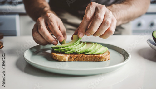 Person arranging fresh avocado slices on toast in bright daylight, clean composition