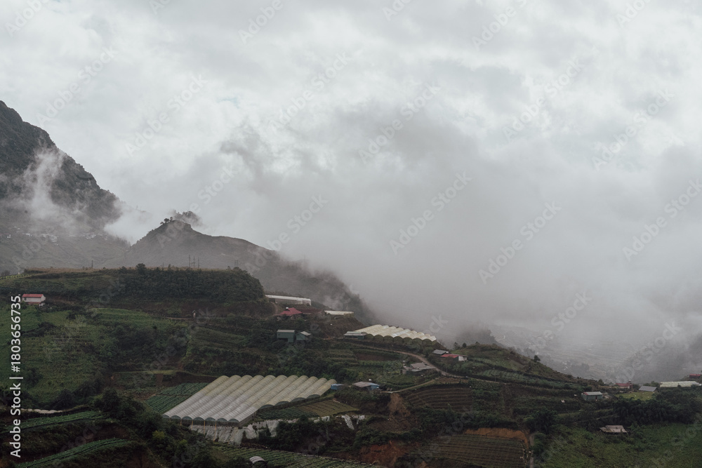 Fototapeta premium Foggy Mountain Valley with Greenhouses and Terraced Fields in Sa Pa, Vietnam