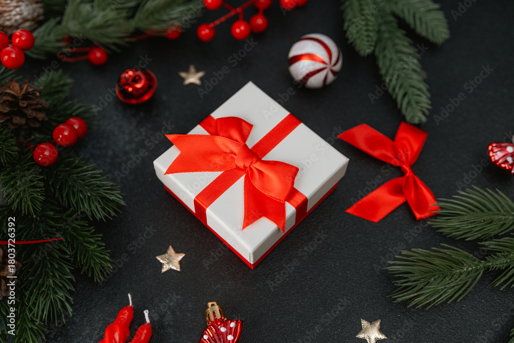 Fototapeta premium Gift box with red ribbon, pine branches, berries and festive decorations on dark surface