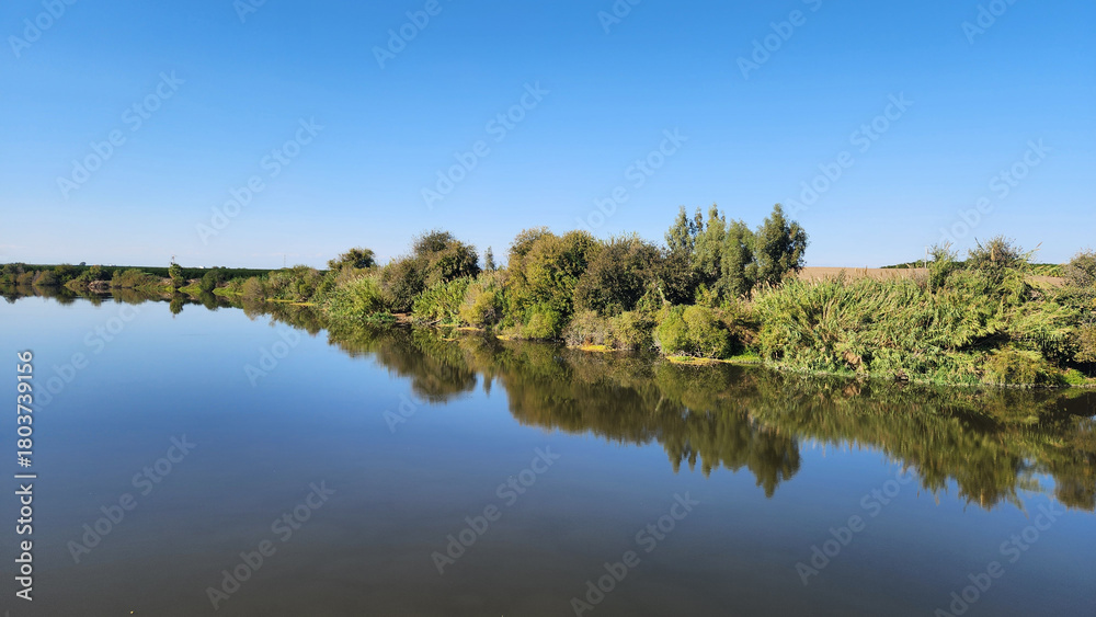 Fototapeta premium In Karataş Adana, Ceyhan River shines under the November sun, its calm waters capturing the colors of autumn