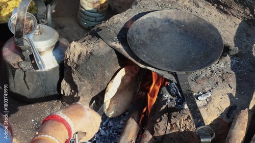 Indian village woman cooking fresh roti on traditional chulha fire with iron tawa