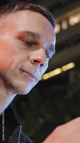 vertical close-up of a handsome Caucasian man typing on a phone, concentrating while texting under the neon glow of a city at night.