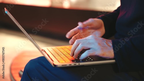 4k close-up of a mans hands actively typing on a modern laptop, streetlights at night. The background is blurred creating a cinematic effect.