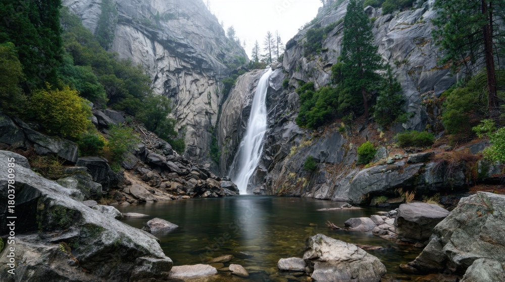 Obraz premium Majestic waterfall cascading down rocky cliffs in a misty forest during a calm morning