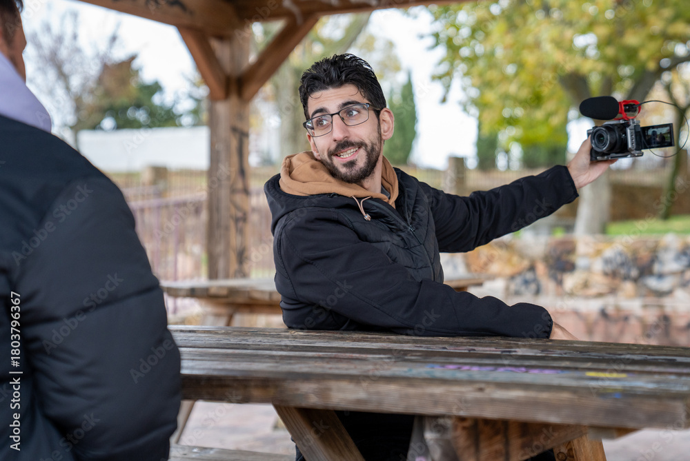 Fototapeta premium Content creator recording video with camera and microphone, interviewing person in outdoor park setting