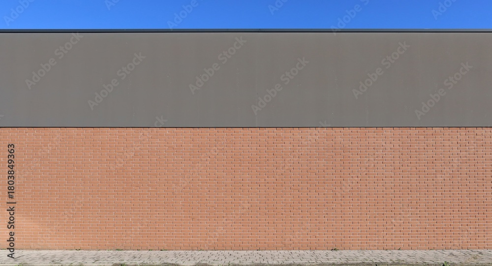 Fototapeta premium Large brick wall with the upper side gray plaster painted. Tiled sidewalk in front. Background for copy space.