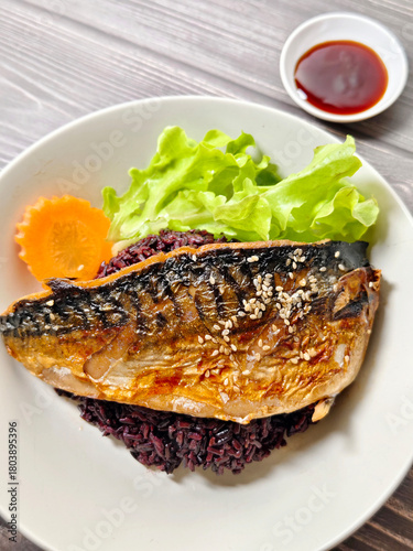 Steamed mackerel with soy sauce served over black rice, garnished with fresh vegetables and sesame seeds, healthy Asian meal.
