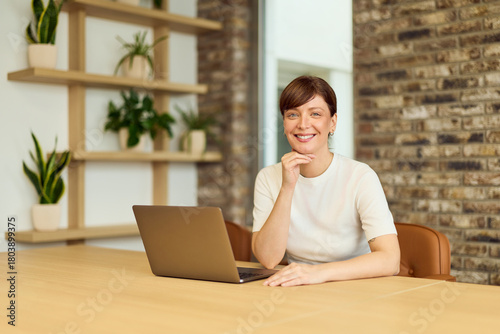 Confident Woman With Laptop At Modern Office Desk Surrounded By Plants