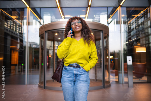 Happy young woman talking on phone outside building