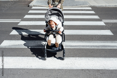 Mother with son in baby carriage crossing street in city on sunny day