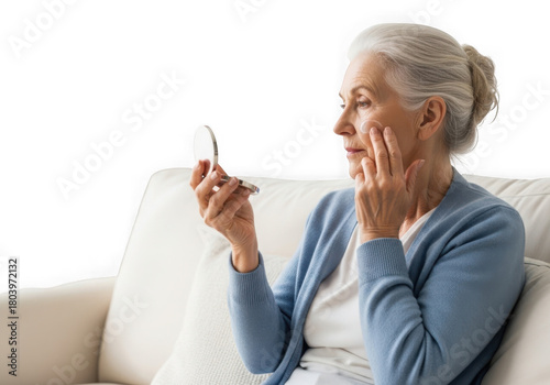 Elderly woman with gray hair checks her face in a small handheld mirror isolated on transparent background