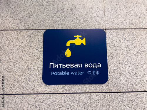 Potable Water sign on wall. Sign in Russian, English, and Chinese indicates the location of the drinking fountain at the airport. International interaction with multilingual signs