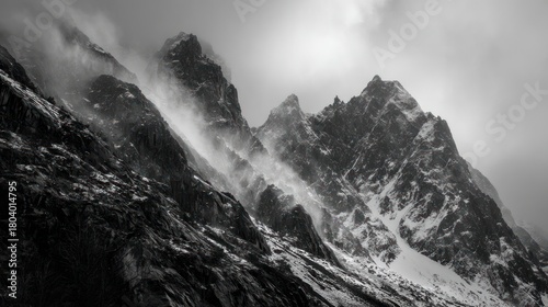 Dramatic monochrome mountain peaks shrouded in mist and light snow, stark, imposing