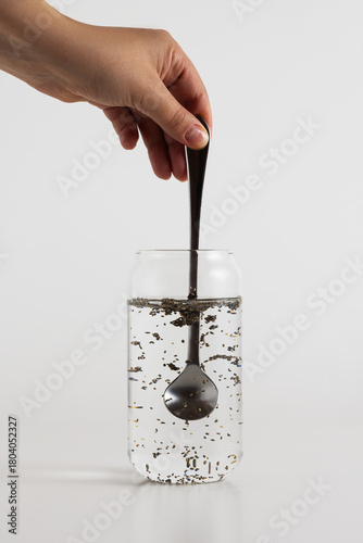 Stirring chia seeds from a silver spoon into a glass of water on a white background
