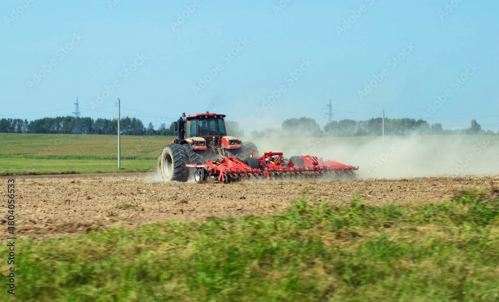 Obraz premium A modern tractor with a new cultivator cultivates the soil in a field before planting crops against a blue summer sky. Agricultural work on a collective farm. Copy space for text