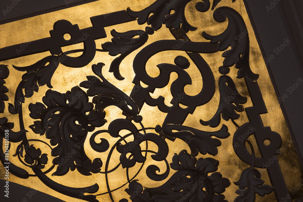 Naklejka premium Intricate black iron scrollwork silhouetted against a rich gold background,