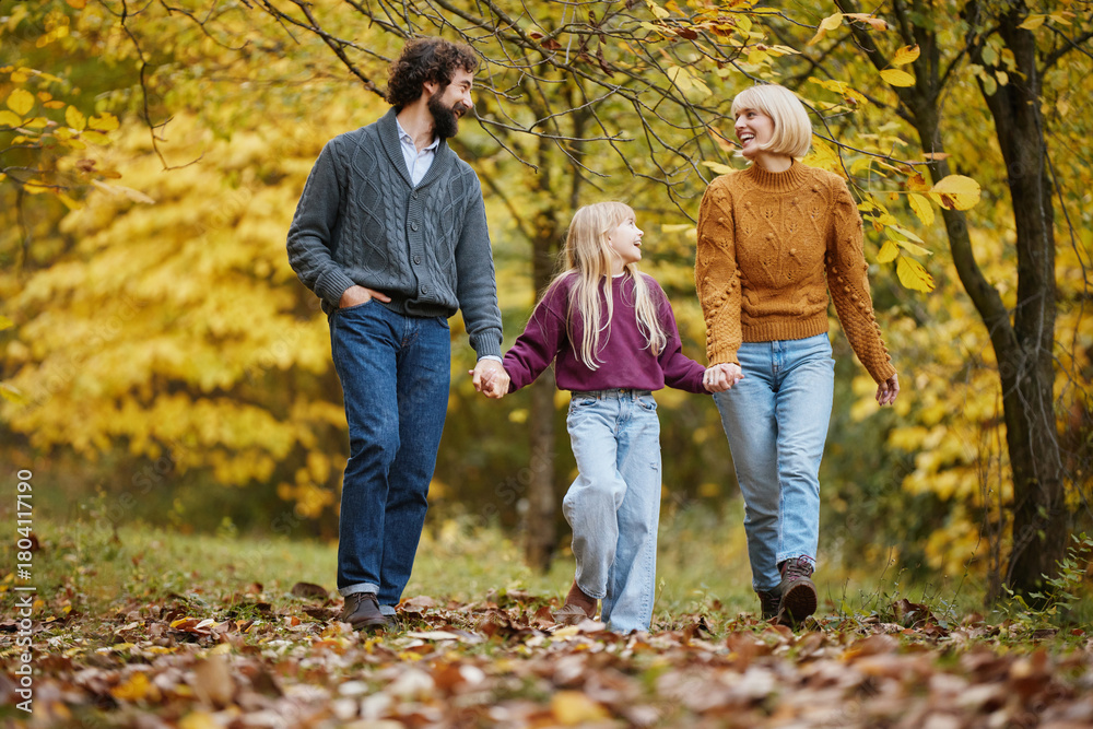 Obraz premium A family takes a leisurely walk in a beautiful park during autumn, enjoying each other's company amidst falling leaves and striking colors.