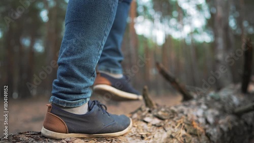 Walking on a log across forest floor showing sneaker and shoe foot contact with bark while walking a nature trail during hike outdoor exploration with closeup of sneaker and foot on bark log