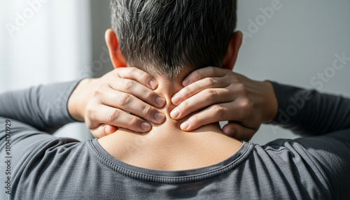 Close-up photo of a person touching the back of their neck, showing visible muscle tension. Soft daylight, clean minimal background. Concept of health, pain relief, and muscle discomfort. High quality