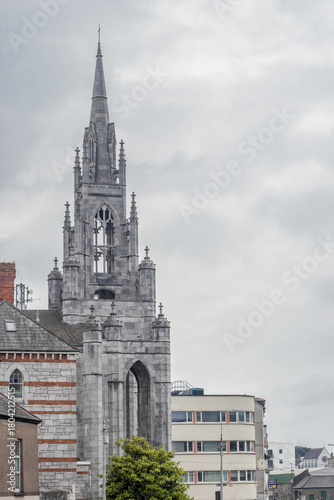 Wallpaper Mural View of a towering grey cathedral spire dominating the skyline, contrasting against the muted tones of surrounding buildings, Cork, County Cork, Ireland. Torontodigital.ca