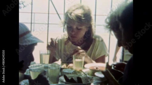 Teenage girl eats with parents at outdoor cafe during summer vacation. Dining in dining room. Family life moment. Group of children, adults together. Old film. Archival retro 1960s. Vintage archive.