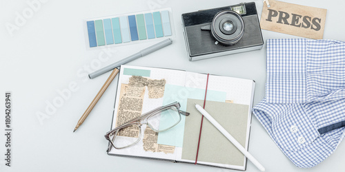 Flat lay of retro journalist essentials on blue background: camera, press badge, notebook