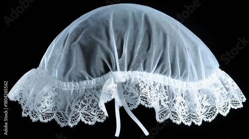 A delicate white lace christening bonnet with intricate patterns and soft ribbon ties, set against a stark black background.