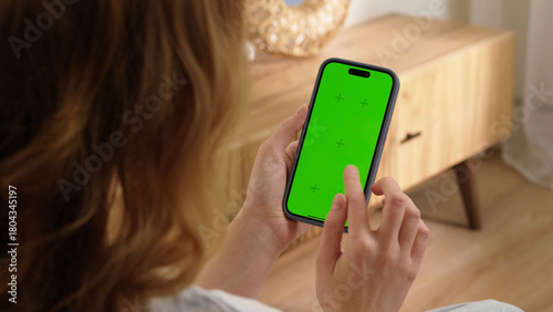 Woman sit use digital tech cell phone with green screen mock up. Hand scroll phone web site, swipe like photos. Girl hold mobile closeup. Chroma key page. Cozy home background. Online app copy space.