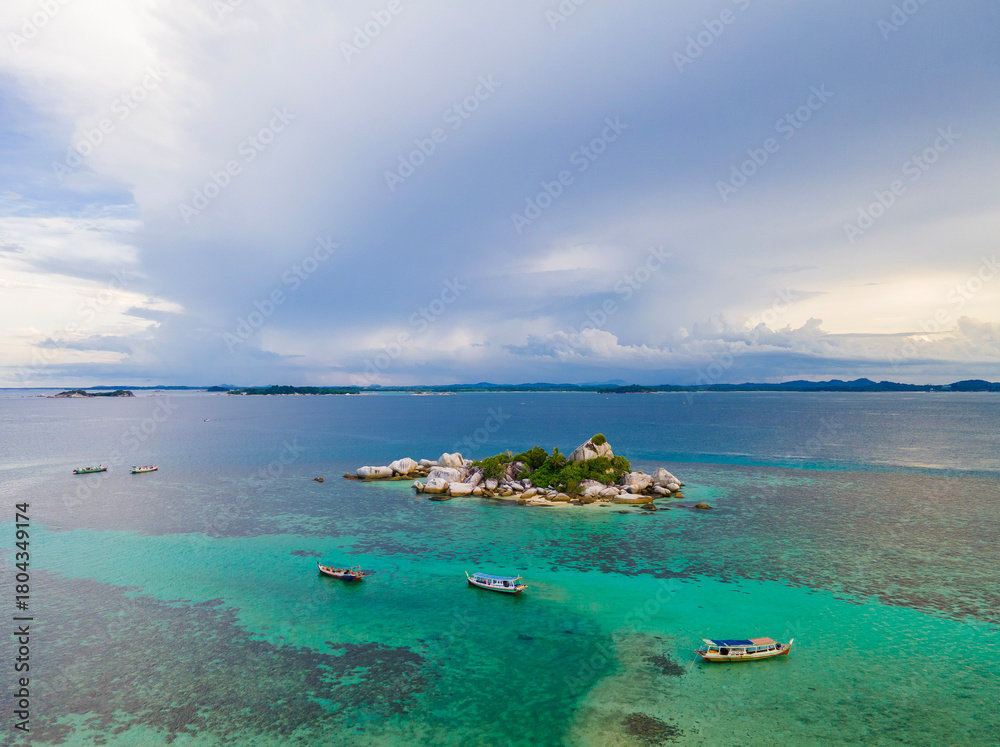 Fototapeta premium An aerial view of a tropical beach in Belitung, Indonesia. Small boats float on the sea, complementing the composition of clear turquoise blue water and small islands with rocks, white sand, and trees