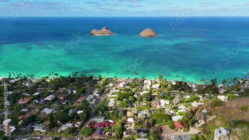 Aerial view of the Mokulua Islands on the turquoise ocean, with lush green trees and houses along the coast, Kailua, Hawaii, United States.