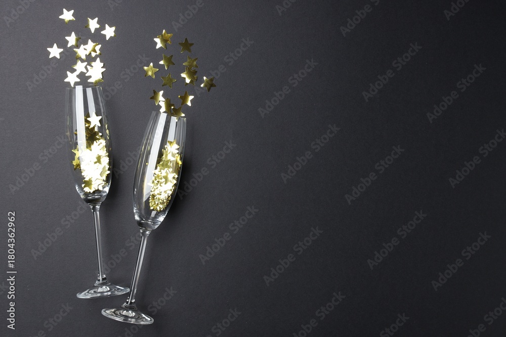 Obraz premium Merry Christmas and Happy New Year. Flute glasses with golden star shaped confetti on black background, flat lay. Space for text