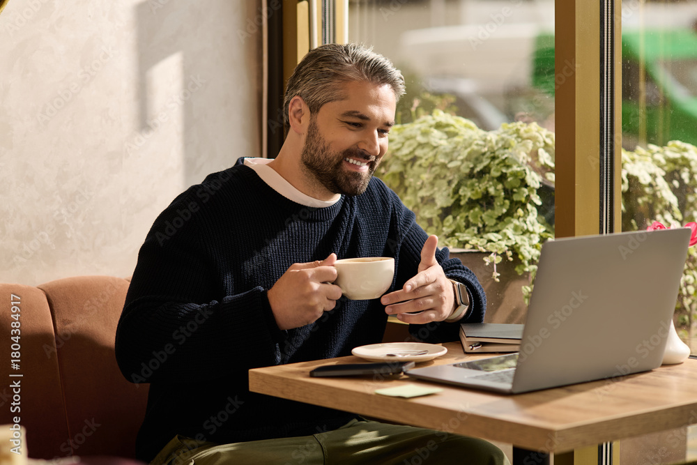 Obraz premium Mature man enjoying coffee at a cozy cafe while working on his laptop