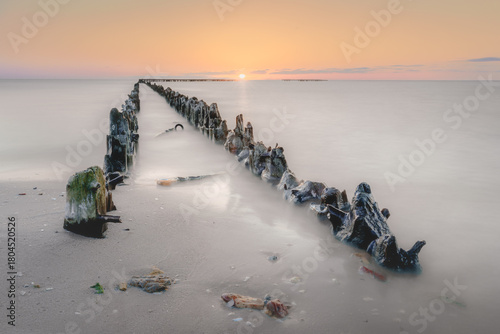 Serene beauty of a sunset seascape, where weathered wooden groynes stretch into calm waters, captured with a long exposure for a dreamlike motion blur.